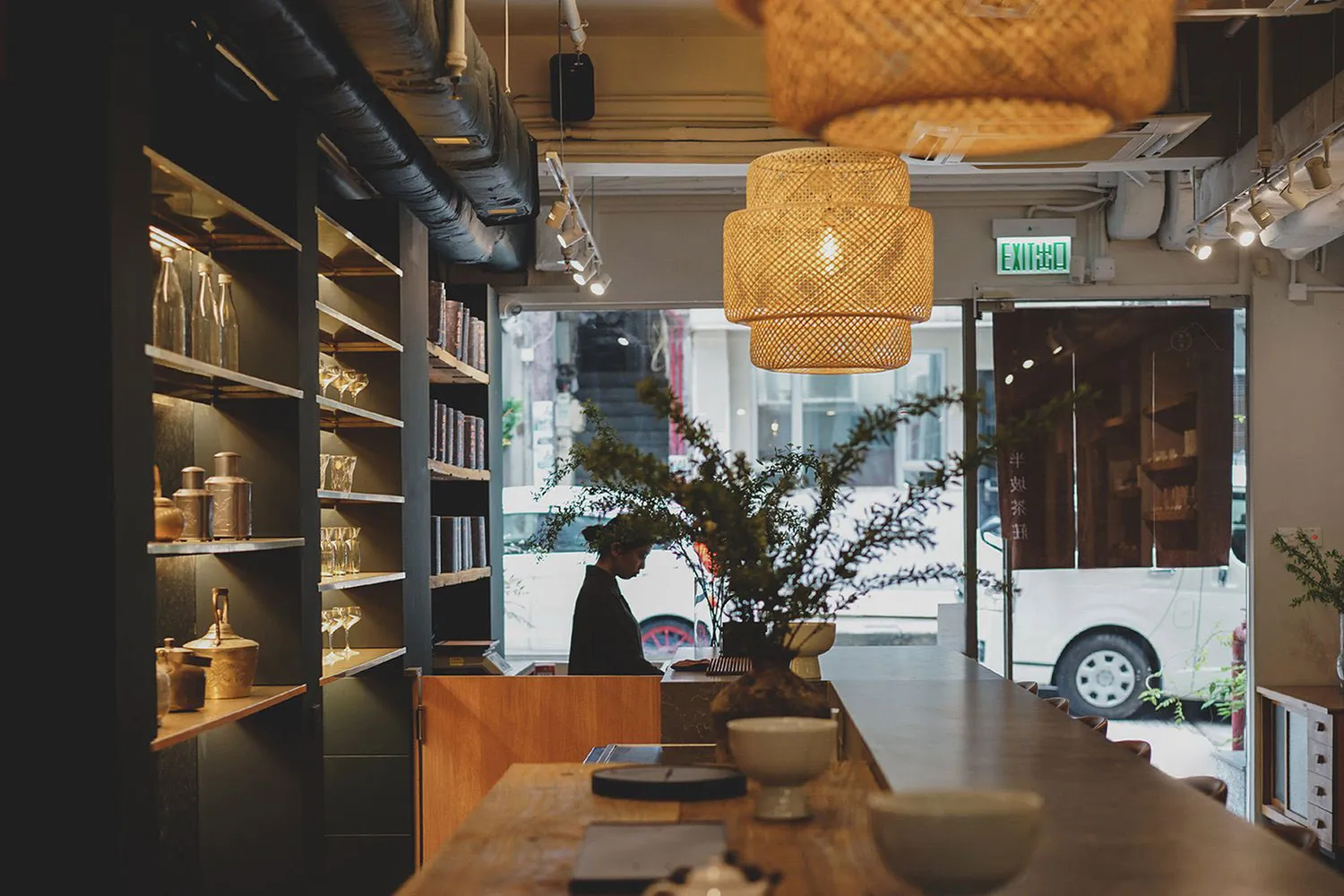 A cozy cafe interior with a counter displaying bowls, cups, and vases, and a person attending to customers