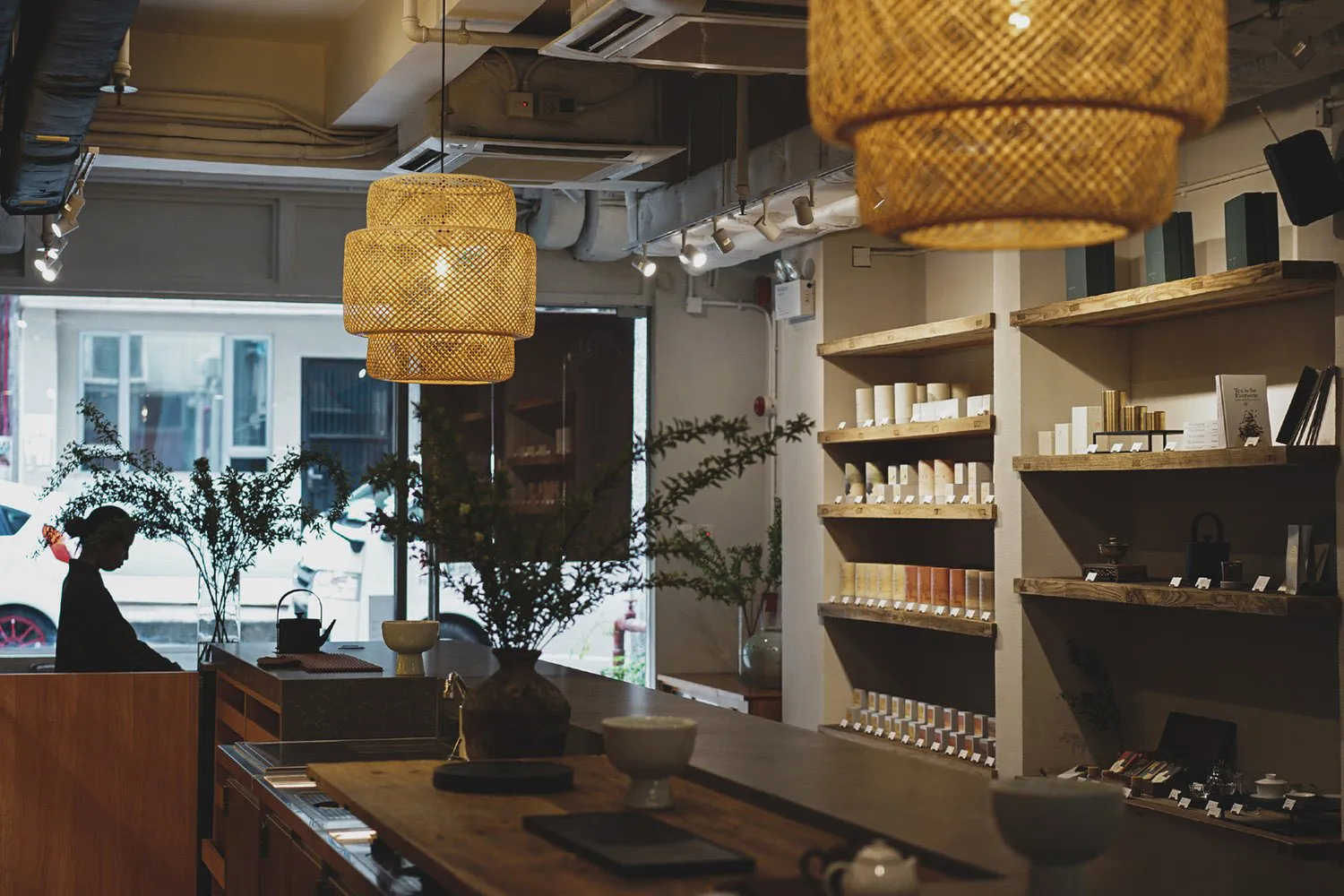 A home decor store with wooden elements, white walls, and hanging lamps, featuring a display of vases, bowls, cups, bottles, and books