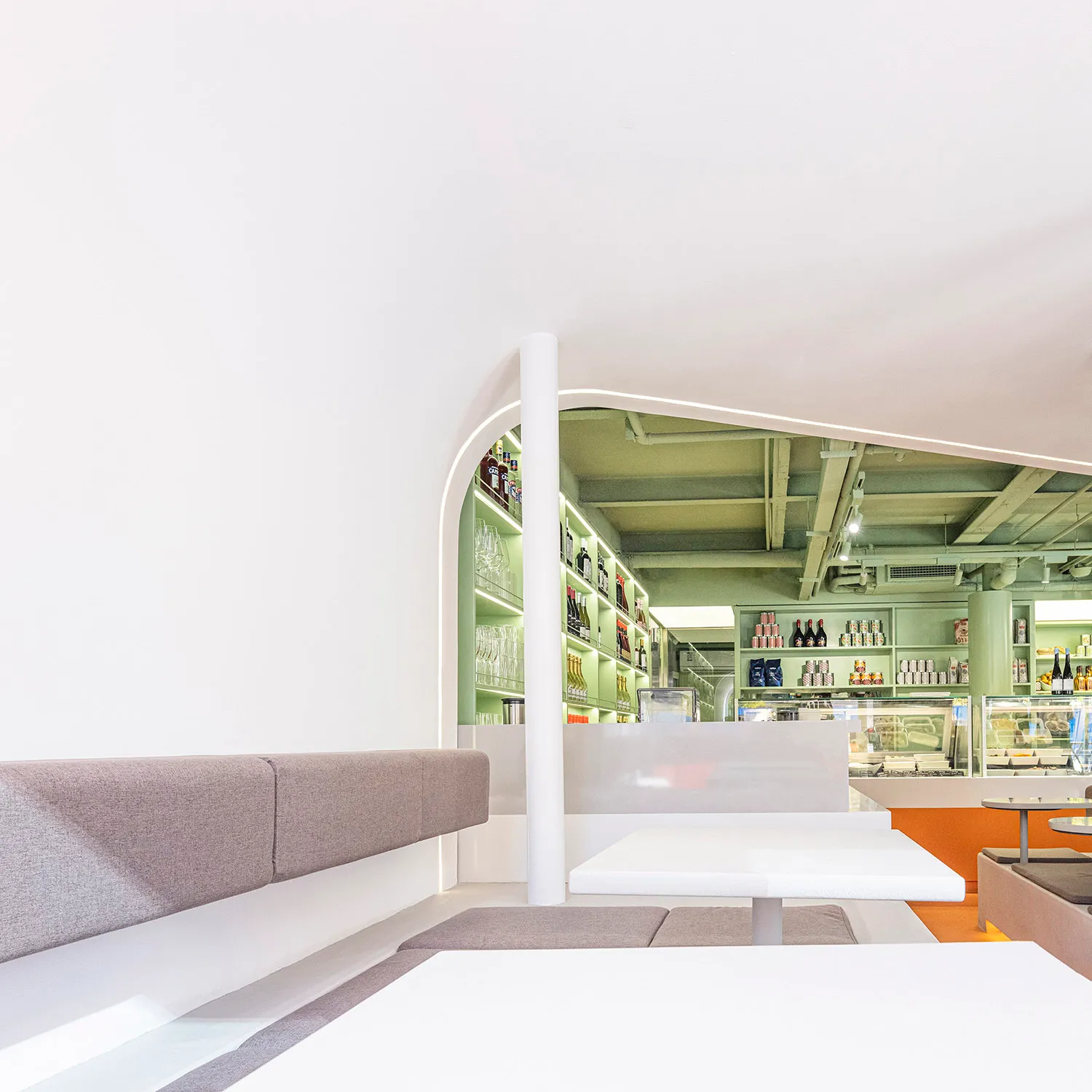 A casual restaurant interior with a large concrete wall, tables, chairs, bottles, and wine glasses, creating a relaxed atmosphere for socializing and dining