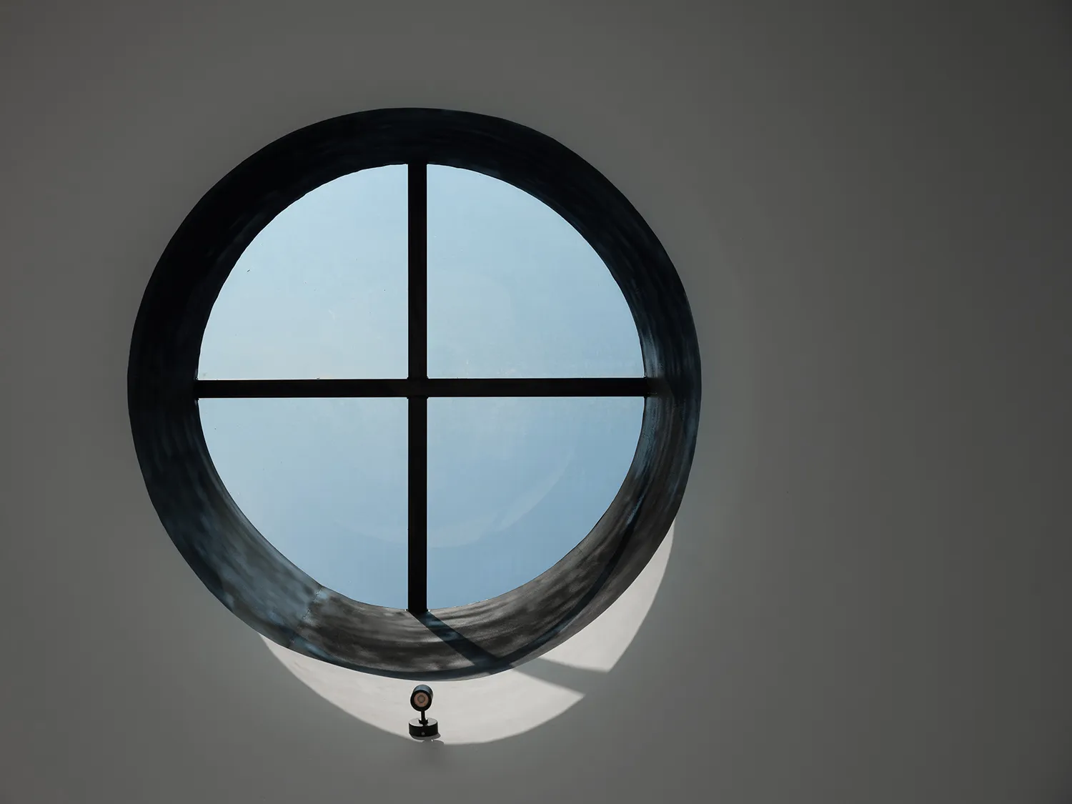 A dimly lit scene with a round window featuring a black frame and a small lamp inside