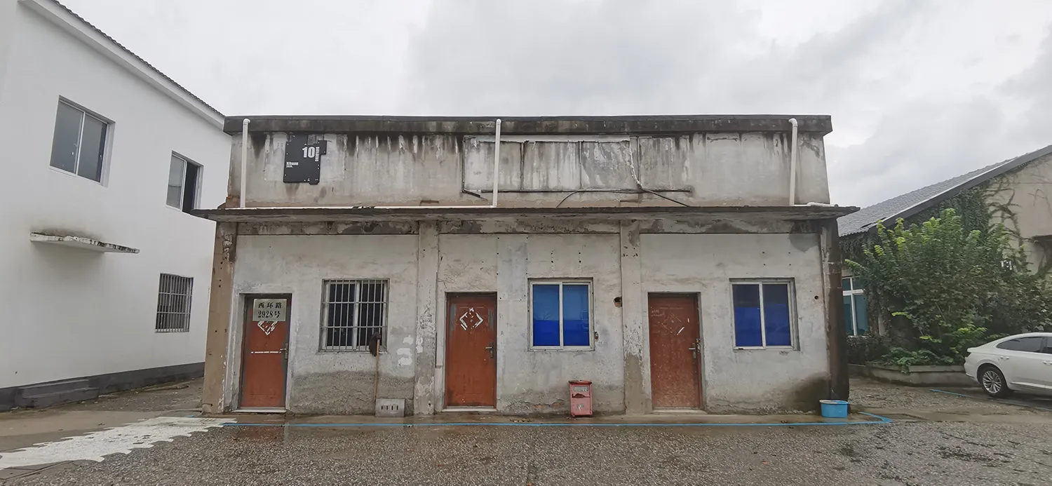 風化混凝土立面的老舊建築，擁有兩扇門與兩扇窗，呈現荒廢模樣