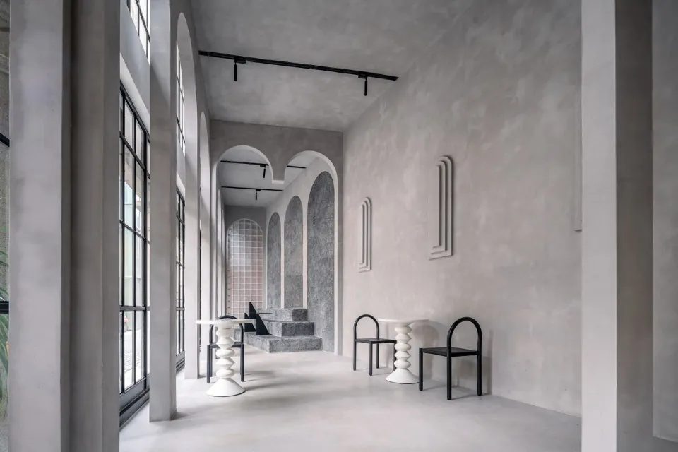 Empty white room with high ceilings, an archway, two chairs, and a dining table, exuding a minimalist and clean atmosphere