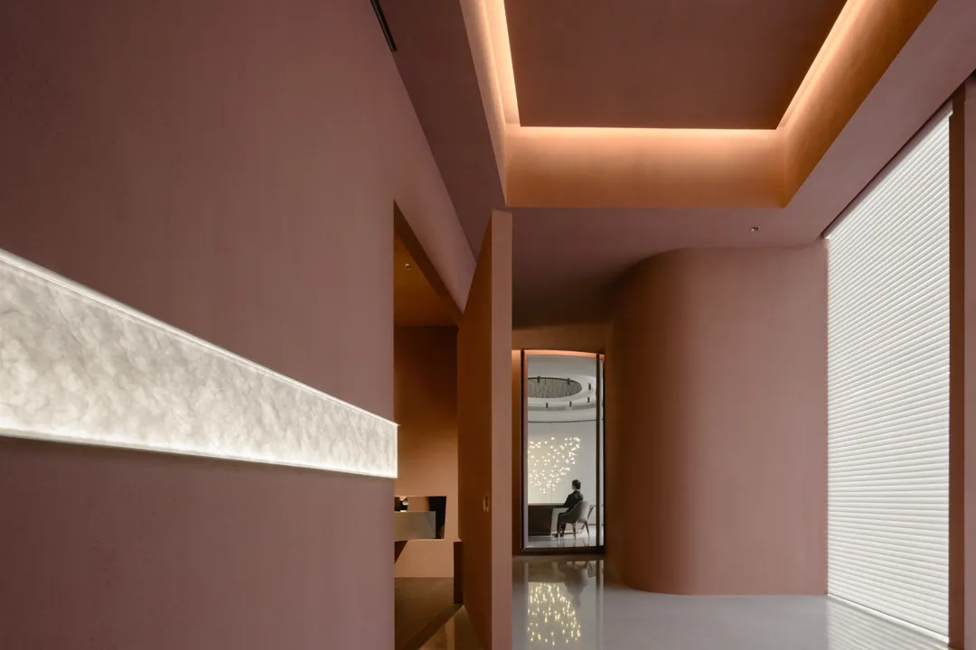 A warm and inviting hotel lobby with a pink accent wall, a chair, and two people, one sitting and one standing