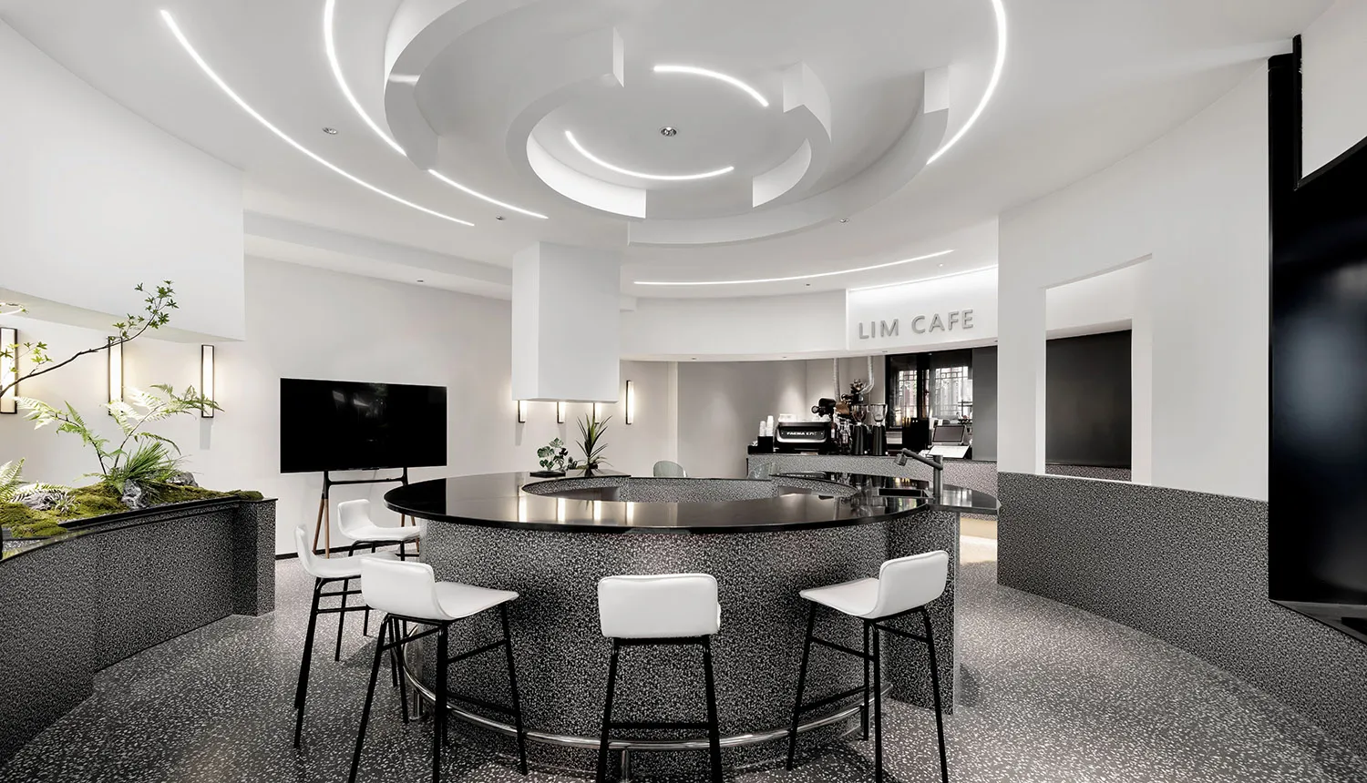 A cozy cafe with a circular bar surrounded by chairs and tables, featuring potted plants and an inviting atmosphere