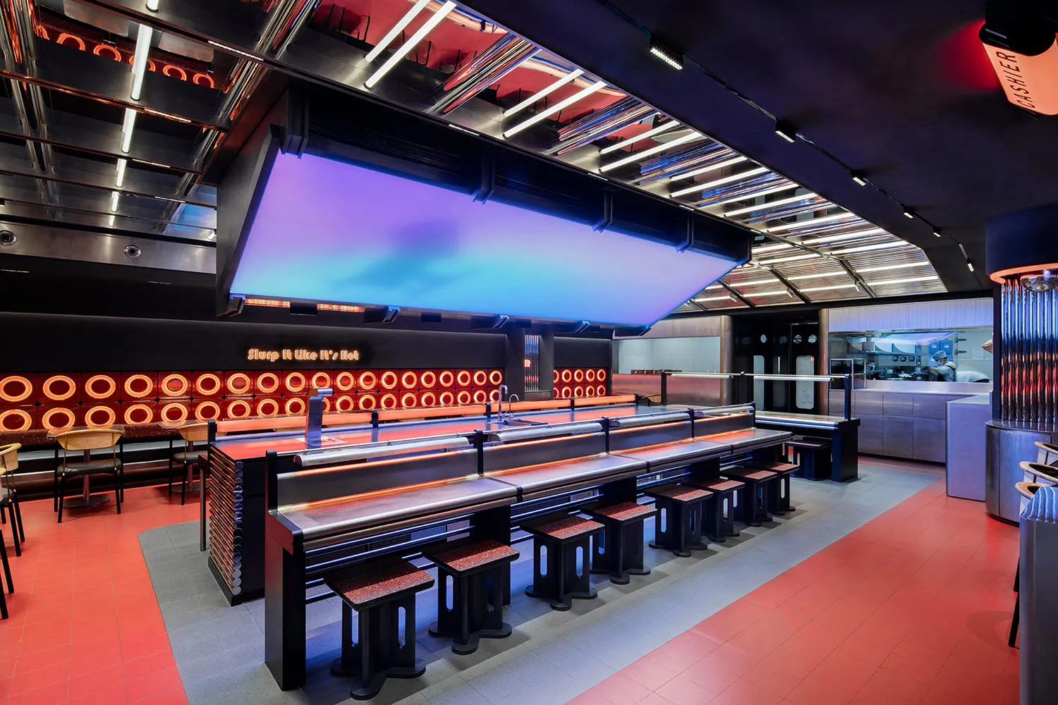 Industrial kitchen with a long countertop featuring multiple stools, multiple sinks, and a modern functional design