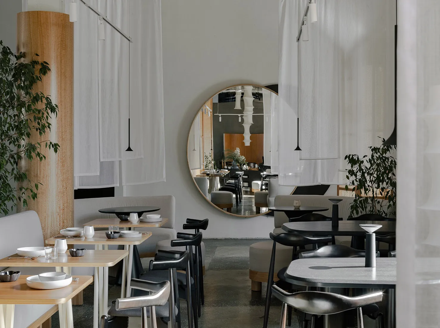 Modern restaurant interior with dining area, tables, chairs, and potted plants, featuring a comfortable and inviting atmosphere