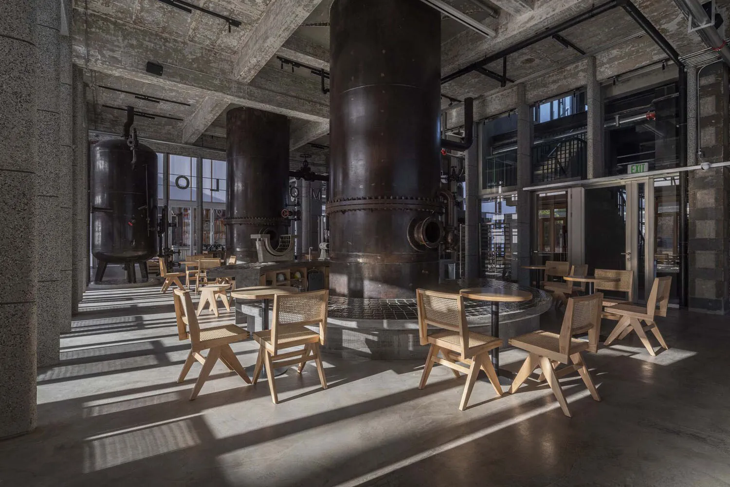 Industrial cafe with cylindrical tanks, chairs, and dining tables, surrounded by benches for social seating