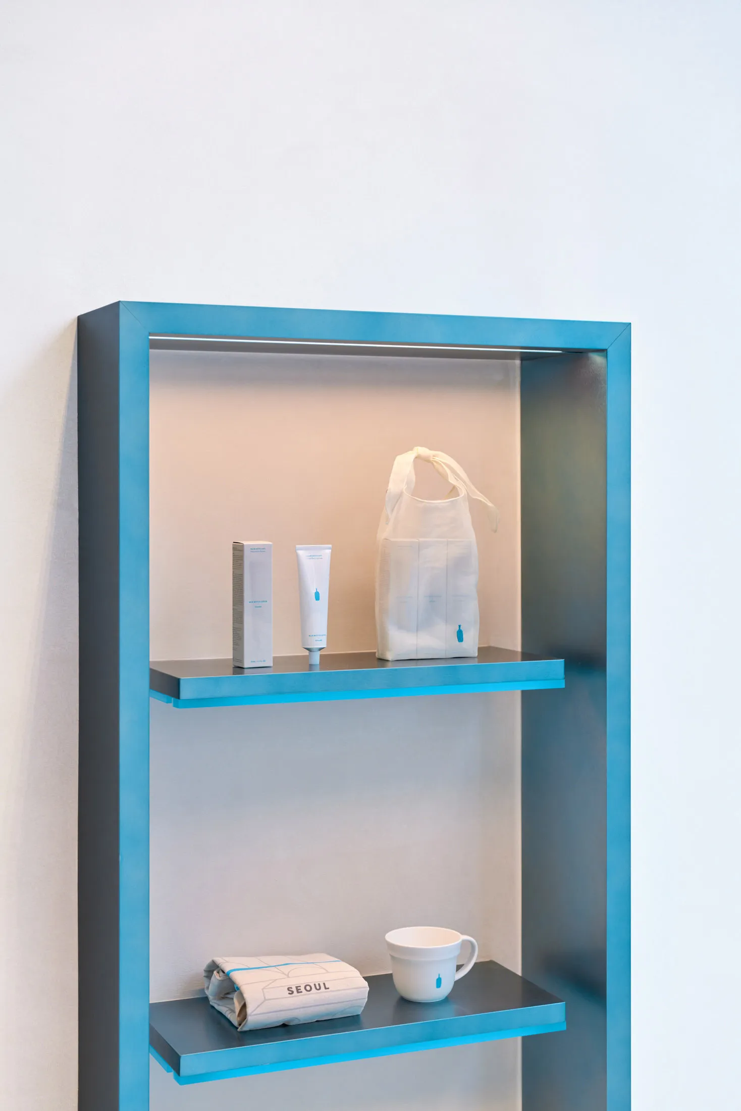 A clean and organized bathroom with a blue shelf holding two bottles of lotion and two bags, adding a pop of color to the neutral space