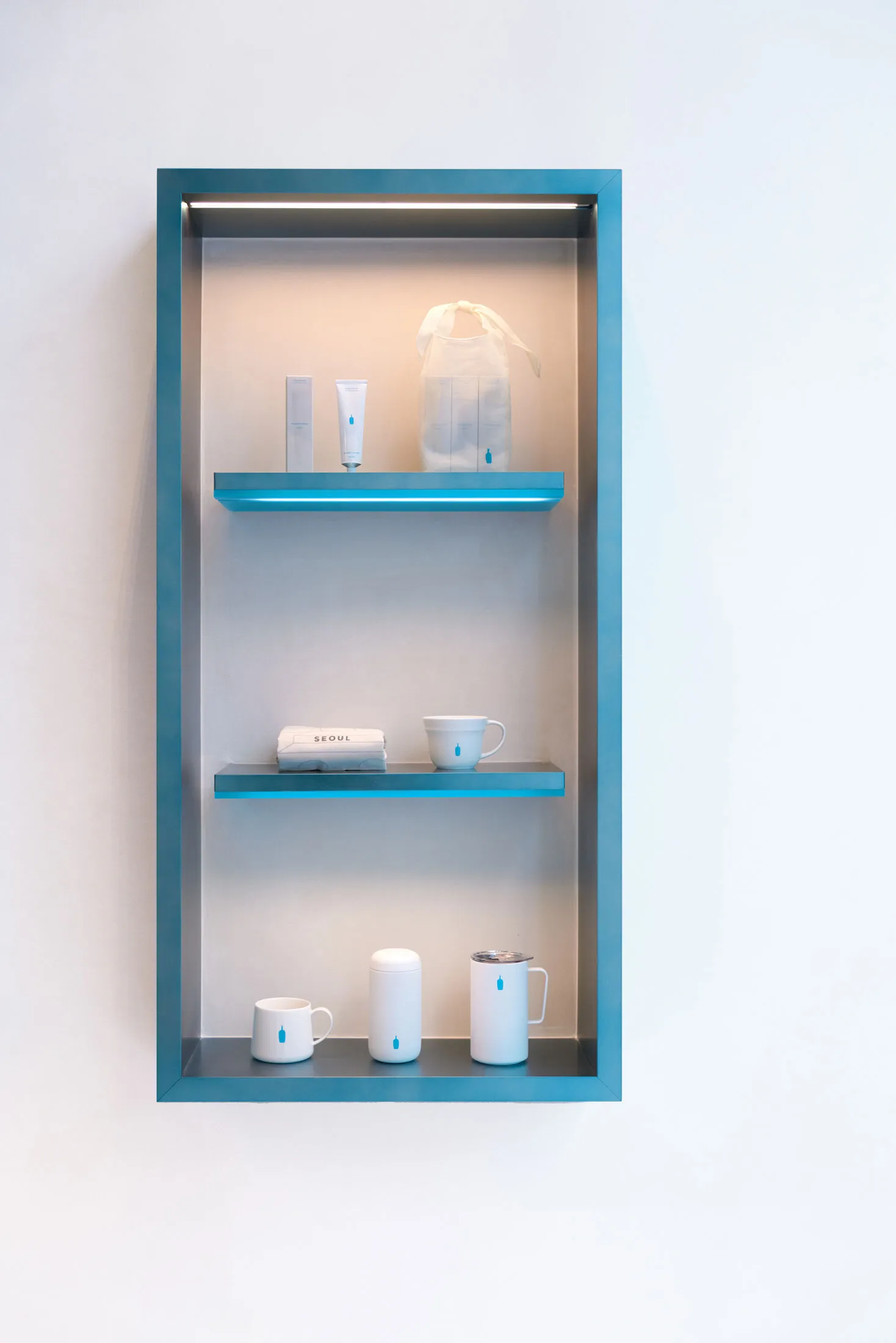 A glass display case filled with three cups, two bottles, and two handbags, arranged in a well-organized and tidy manner