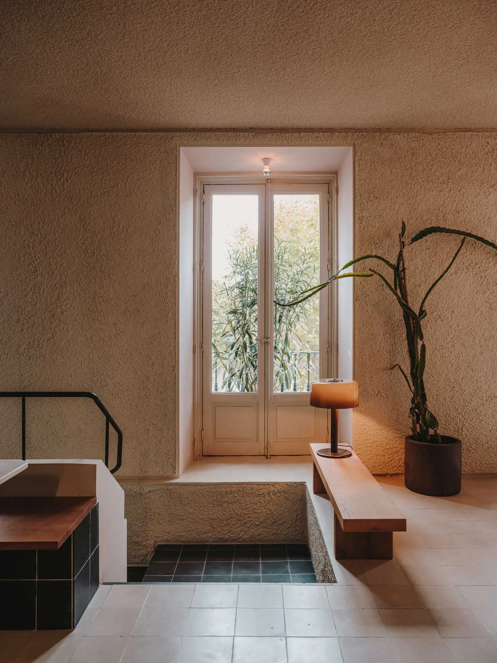 Modern bathroom with a sink, toilet, and shower area, featuring concrete walls, a large window, and a potted plant