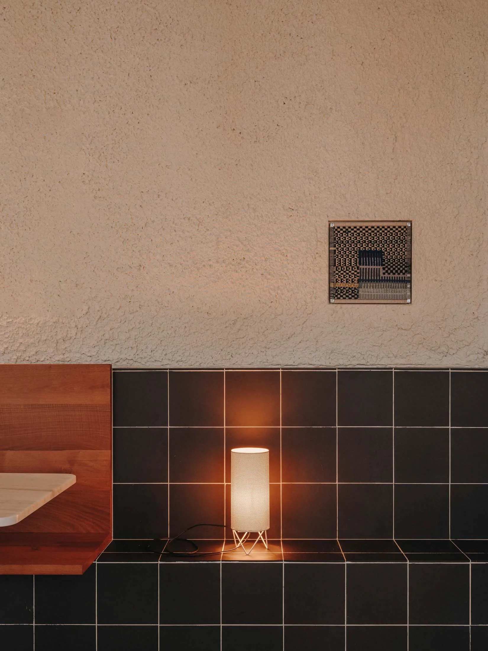A bathroom with a tiled wall and a wooden countertop, lit by two lights, creating a clean and well-lit environment