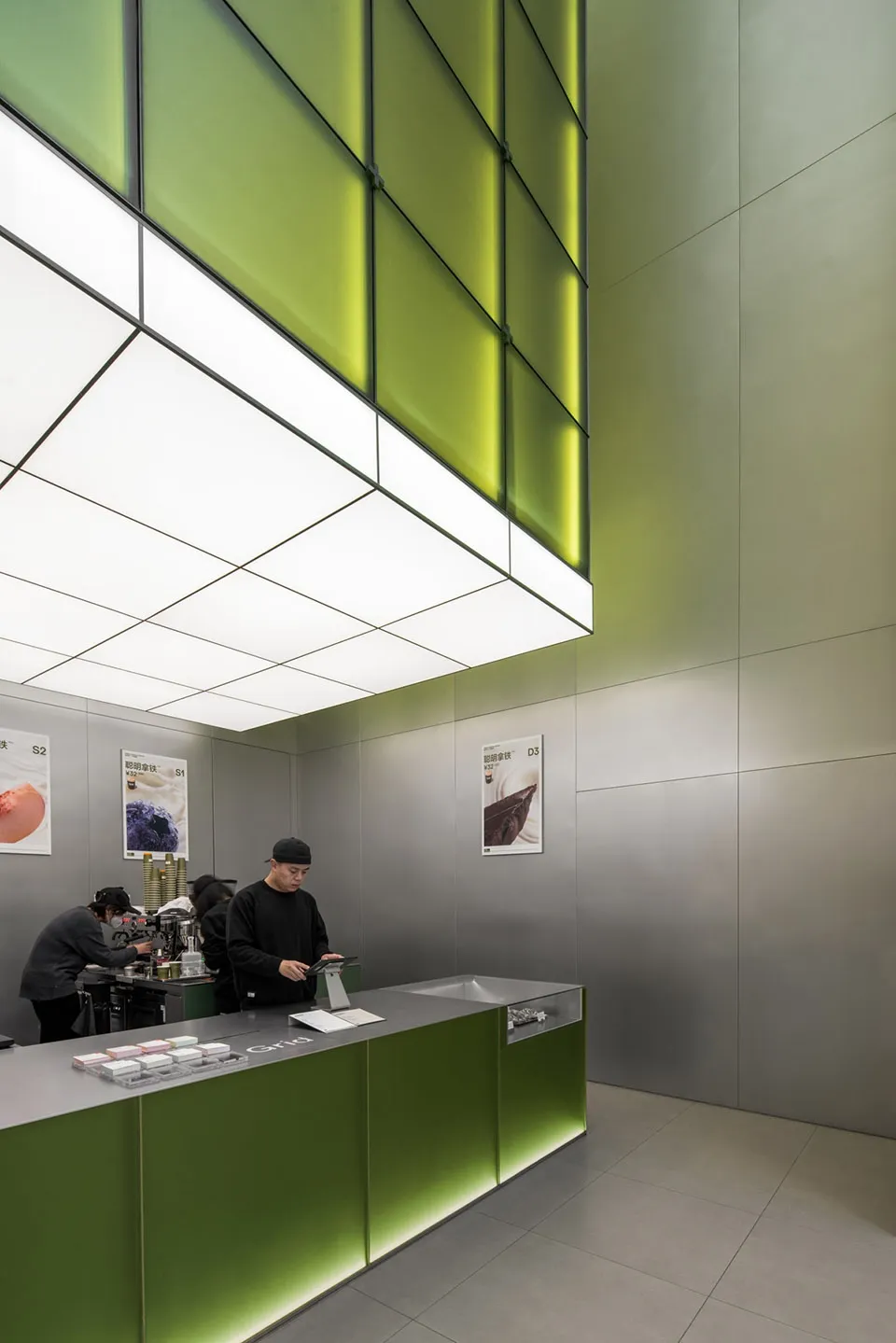 A modern restaurant interior with a metal counter, green walls, and customers ordering food and drinks