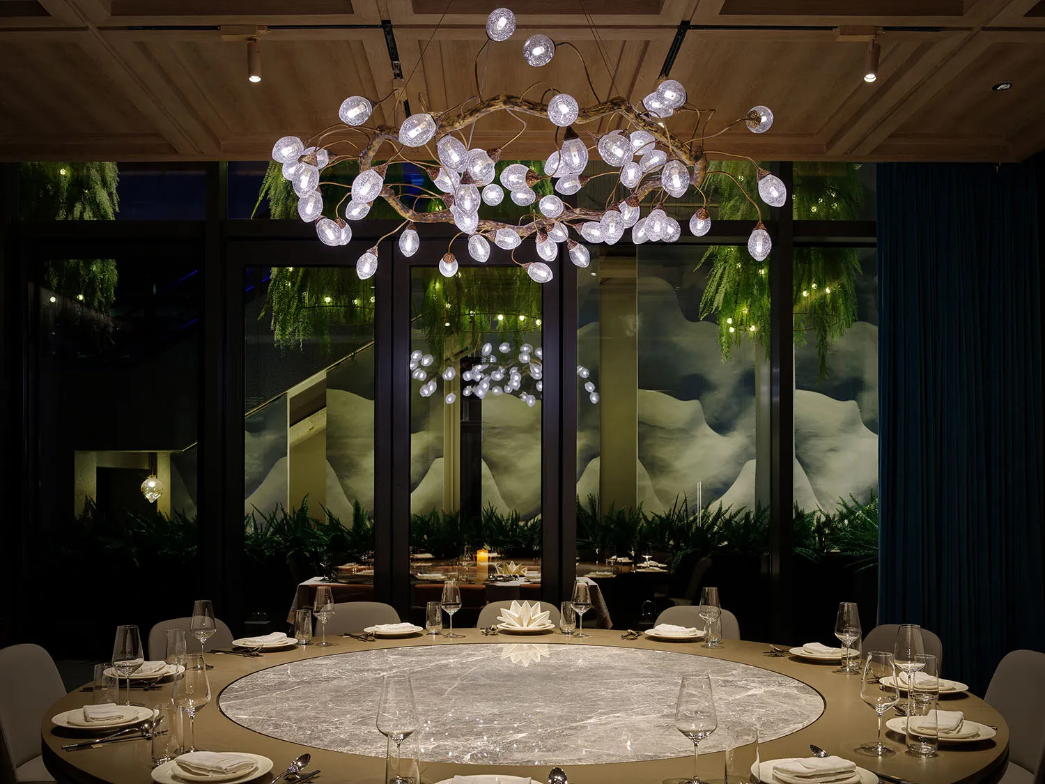 A sophisticated dining space with a large glass table surrounded by chairs, wine glasses, and cups, set in a well-lit room