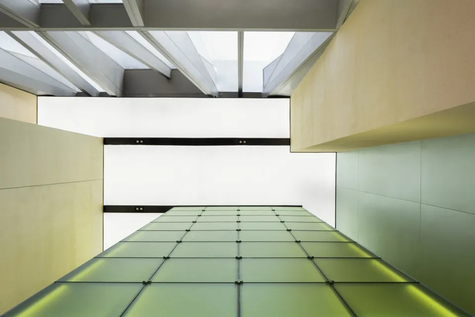 A modern interior space with a large green-tinted glass wall extending upwards, creating a sense of openness and spaciousness