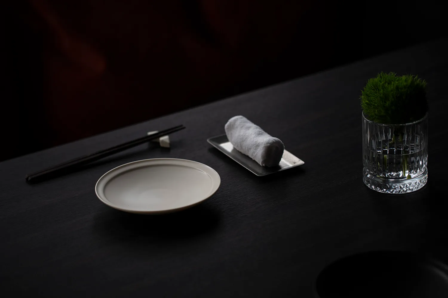 A dark room with a wooden dining table featuring two bowls, chopsticks, and a vase, creating an intimate ambiance