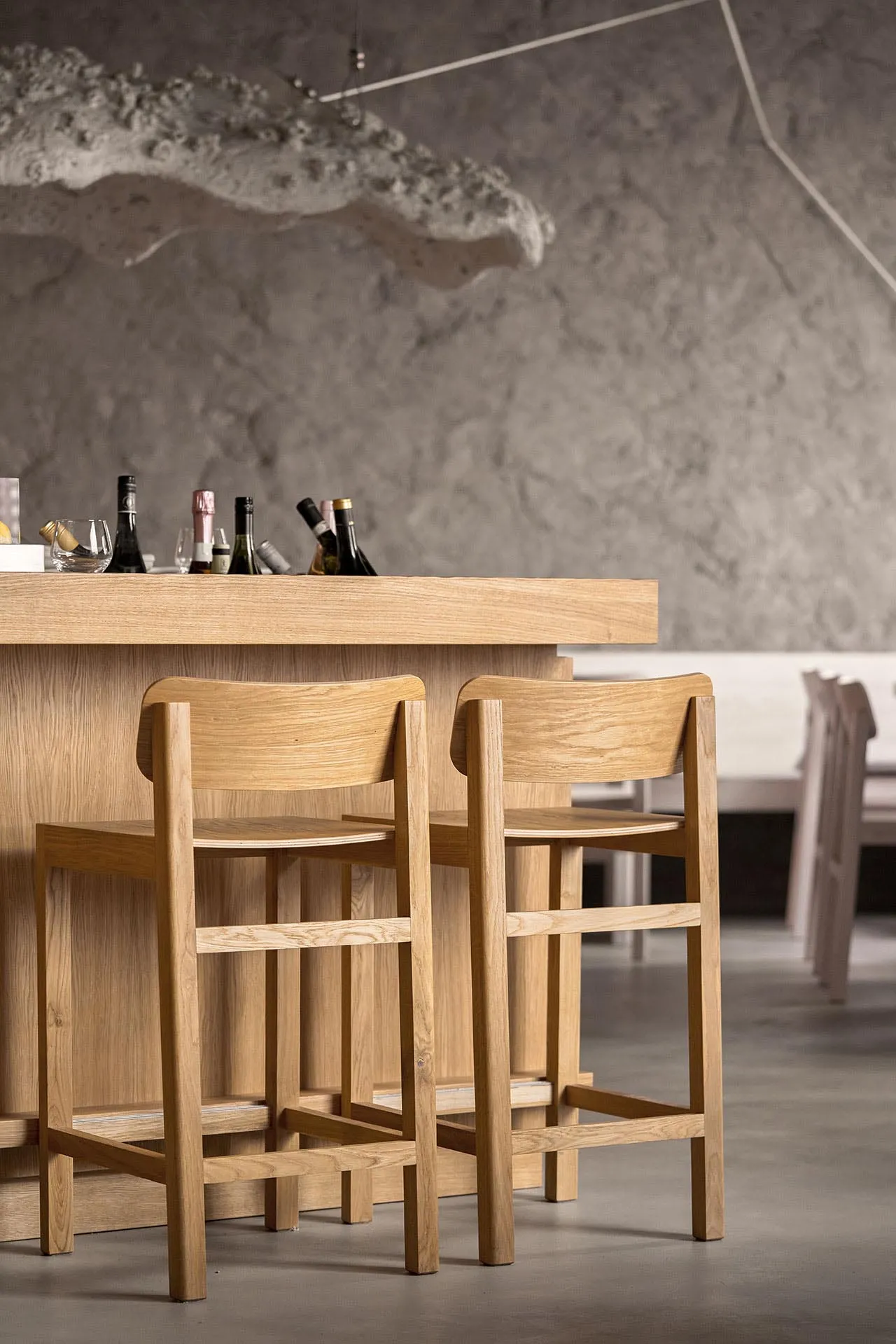 An empty bar area with wooden stools and tables, featuring a selection of bottles on the counter, creating a calm and inviting atmosphere