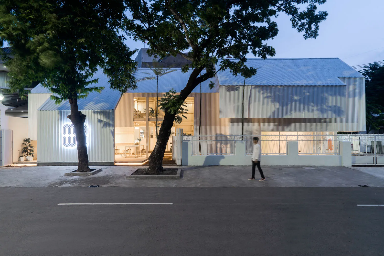 A modern building with a large window on its side, surrounded by chairs and a person walking by, conveying a calm and serene atmosphere