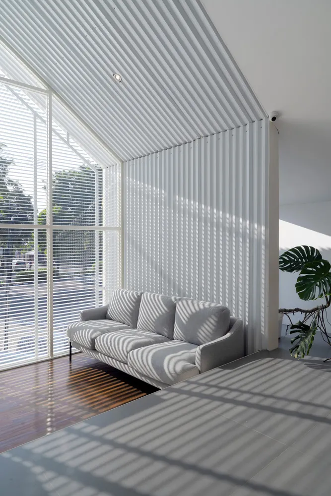 Open living area with a striped sofa, vertical blinds, potted plants, and a chair, featuring natural light and a simple atmosphere