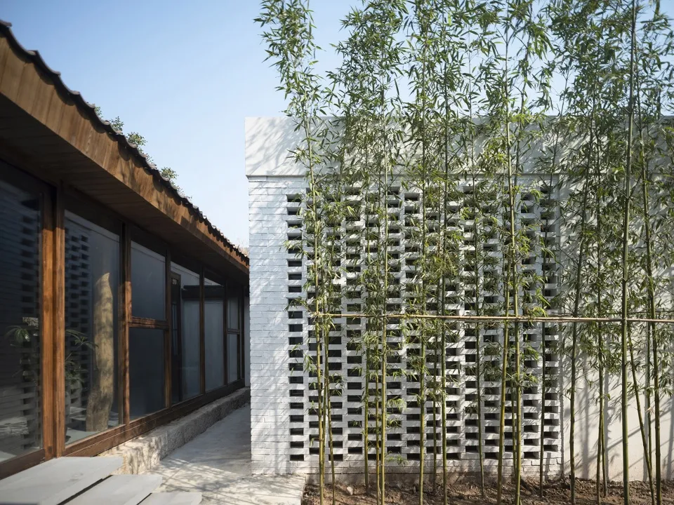 A modern house with a white exterior and a bamboo fence in front, featuring symmetrical windows and a clean design