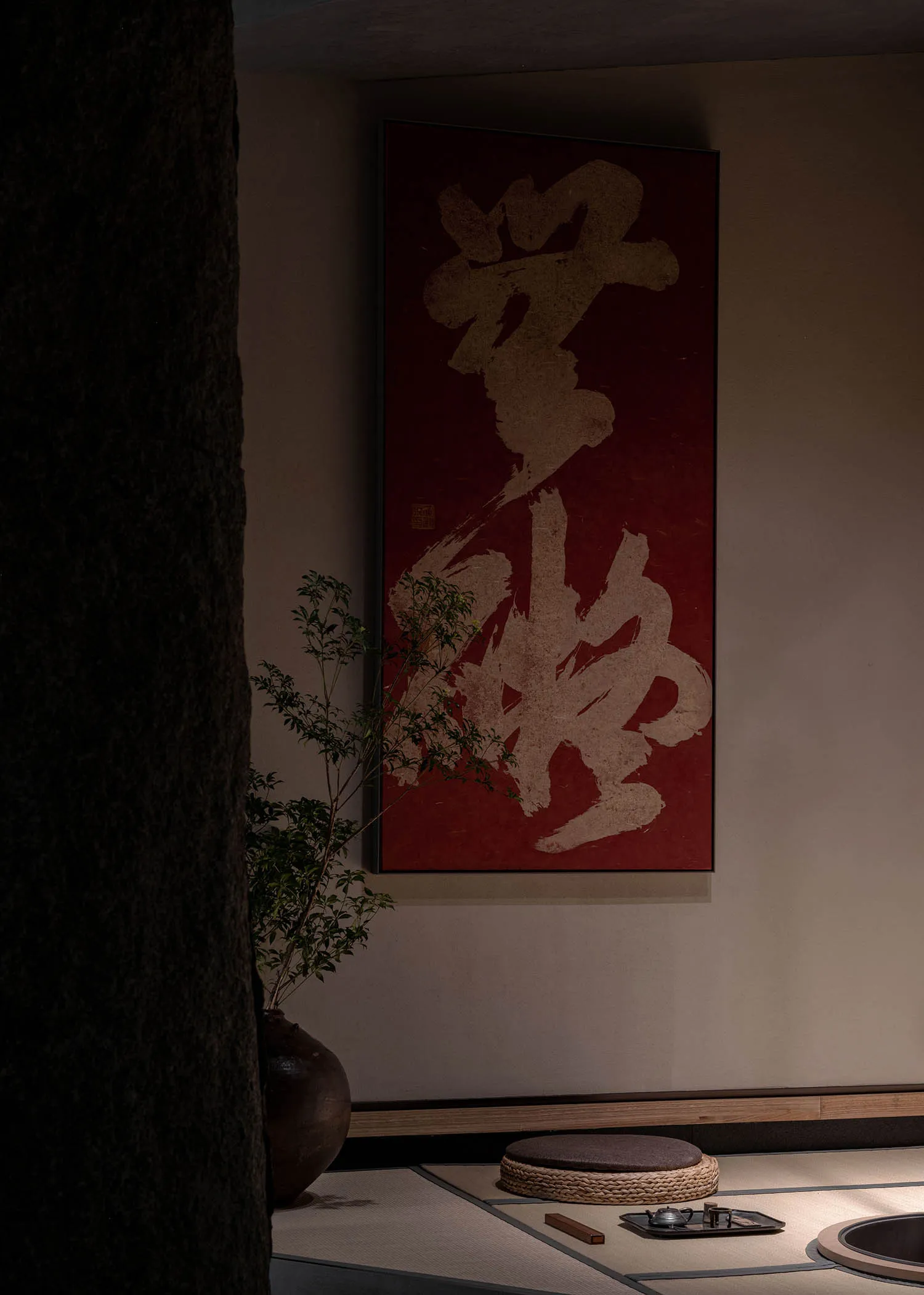 Dimly lit room with a red wall featuring Chinese characters, two potted plants, and a blend of traditional and modern design elements