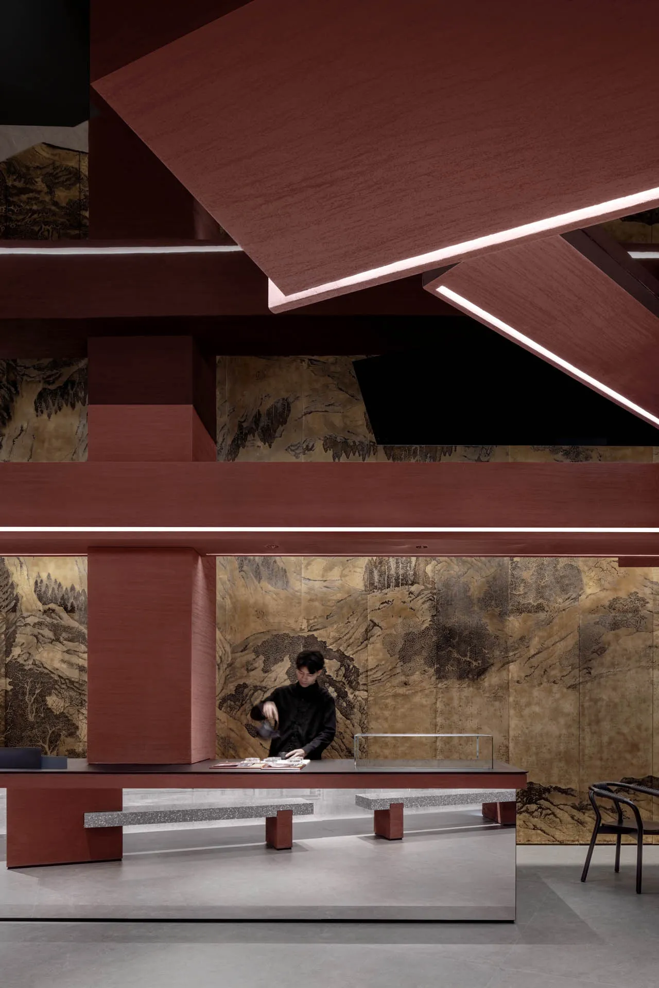 A man prepares food at a wooden counter in an Asian restaurant with a red wall and two chairs