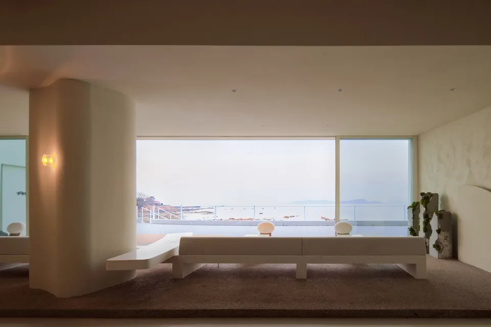 Open living space with large windows offering an ocean view, featuring a bench and two chairs for comfortable seating