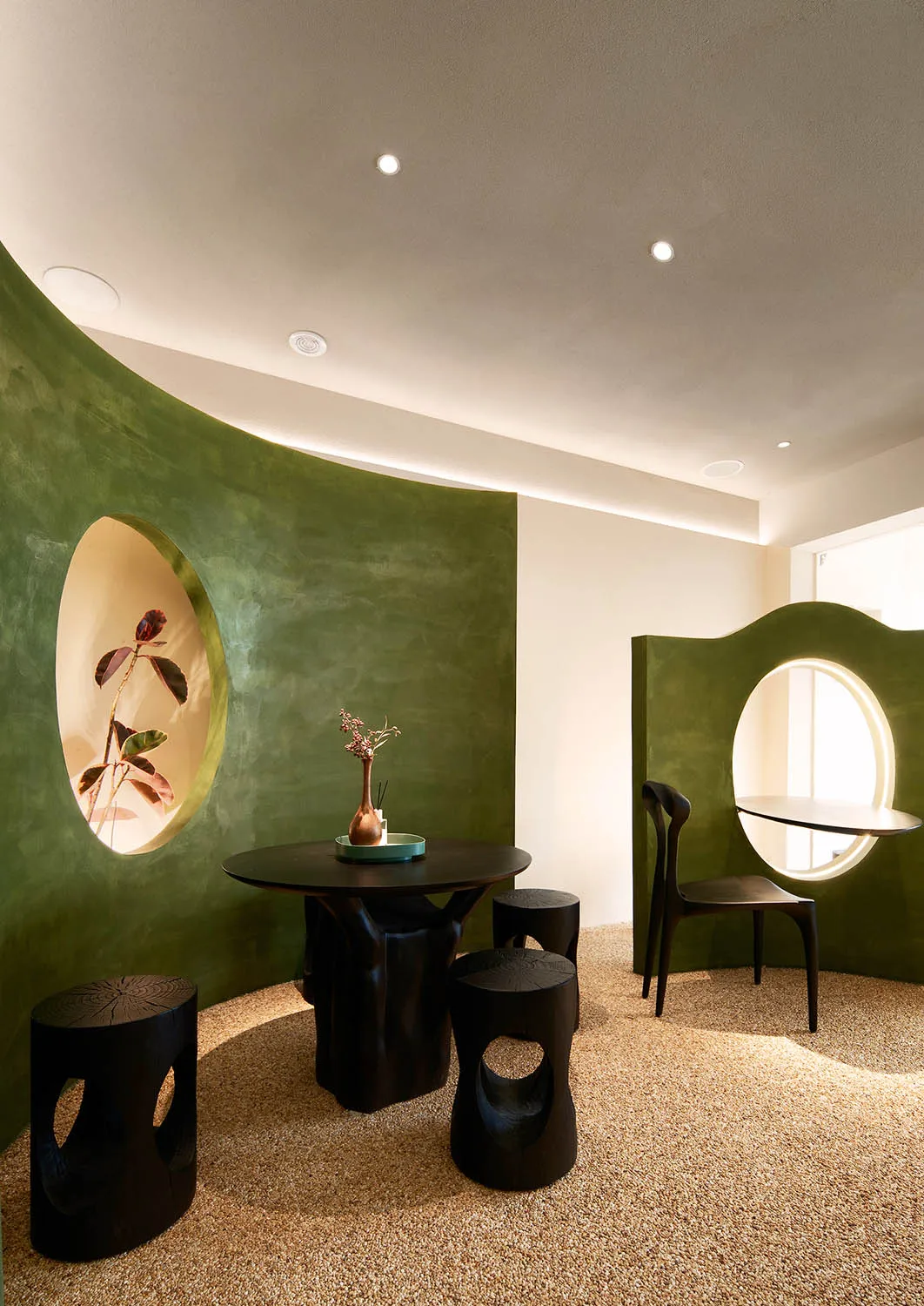 Dining area with a round table, green walls, and a potted plant, creating a cozy atmosphere