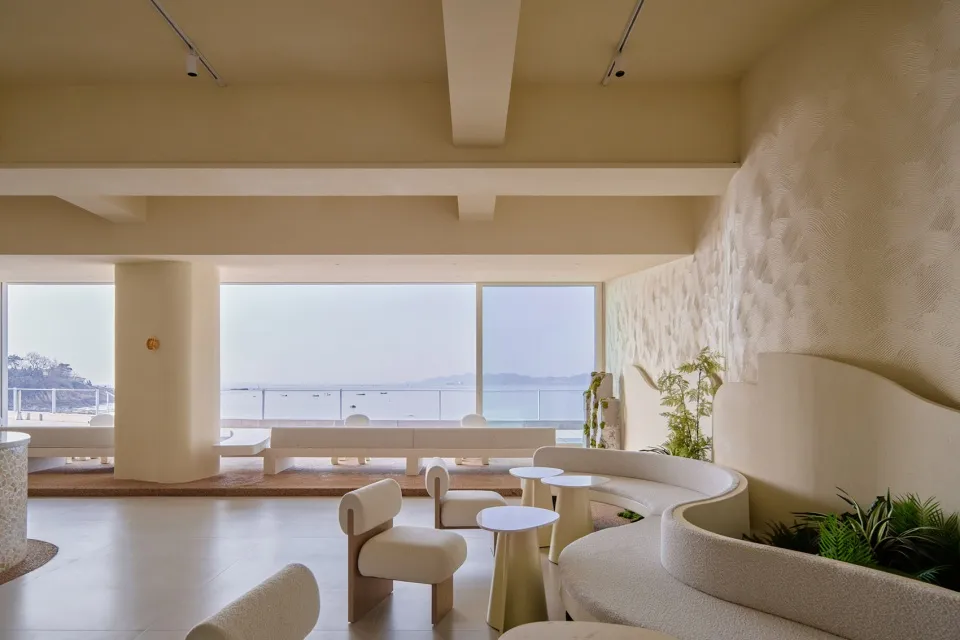 Coastal living room with modern design, white walls, beige furniture, and a large window overlooking the ocean