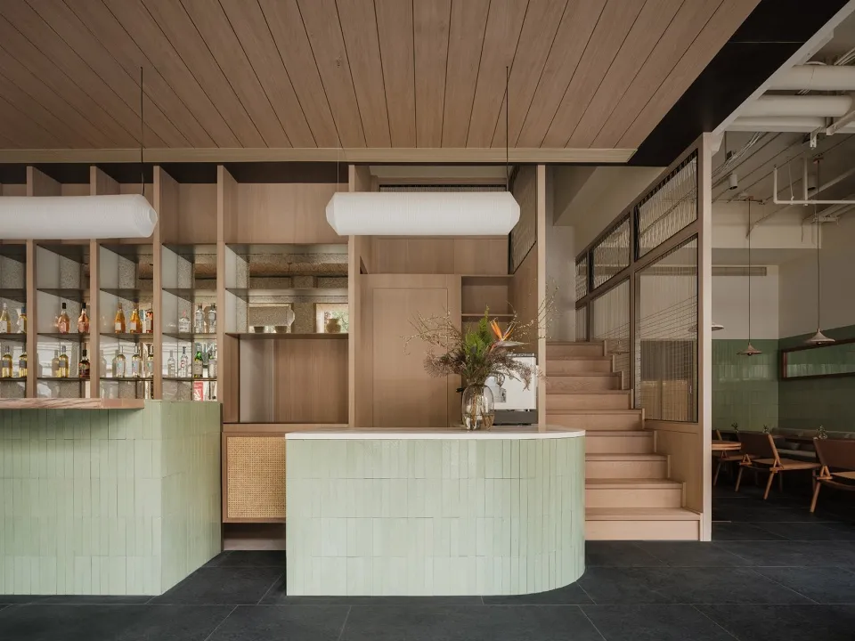 Industrial-style restaurant with wooden floors and walls, featuring two bars with green and white countertops, surrounded by bottles and vases