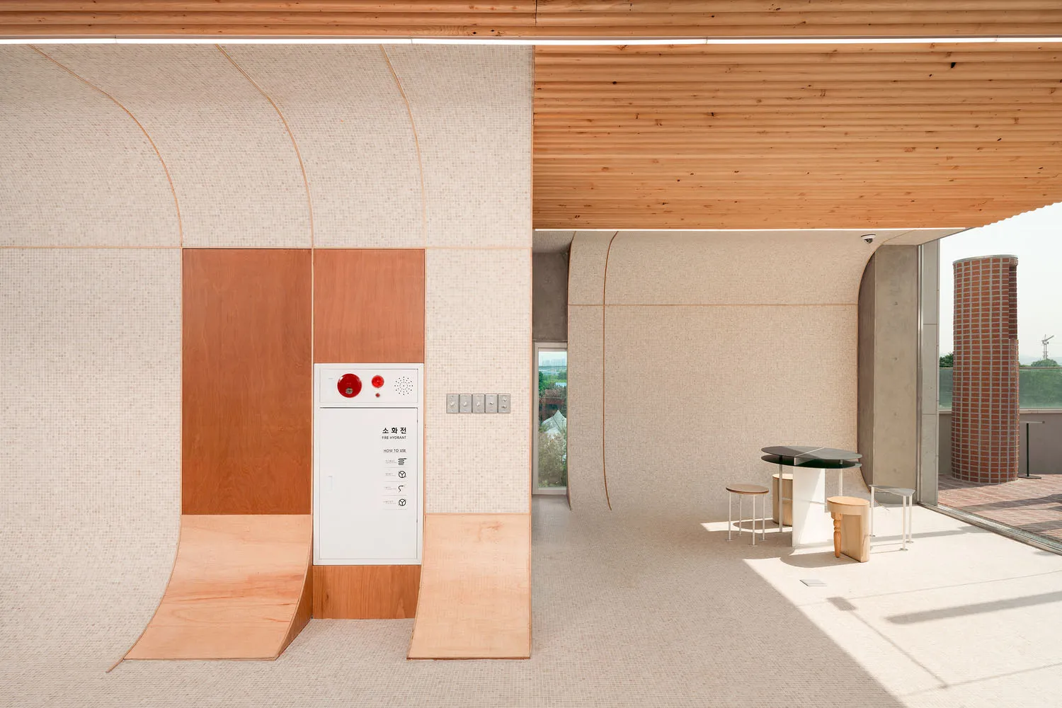 Modern interior space with a white box, wooden wall, two benches, a refrigerator, and a sink, well-lit and minimalist