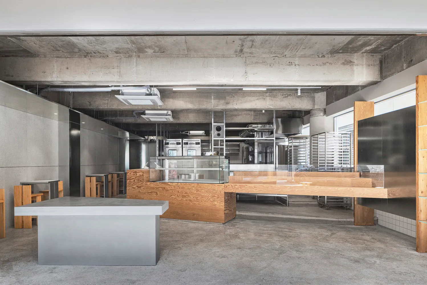Industrial kitchen with a large wooden countertop, sink, ovens, and refrigerator, giving off a modern and sleek vibe