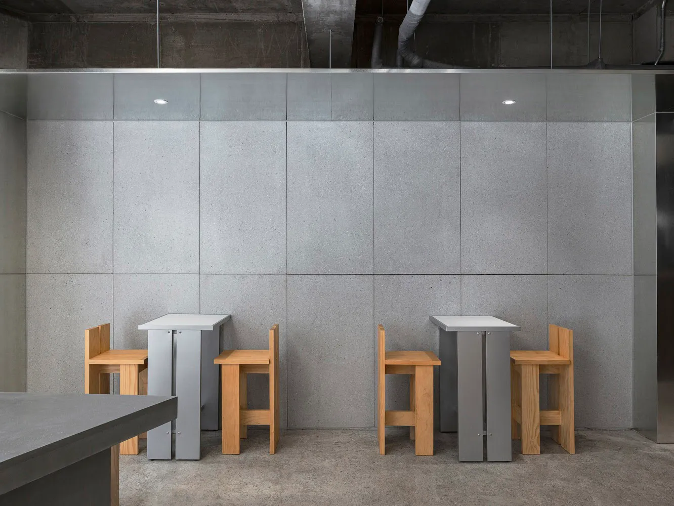 Empty restaurant with two grey tables and wooden chairs in a modern space with concrete walls and a calm atmosphere