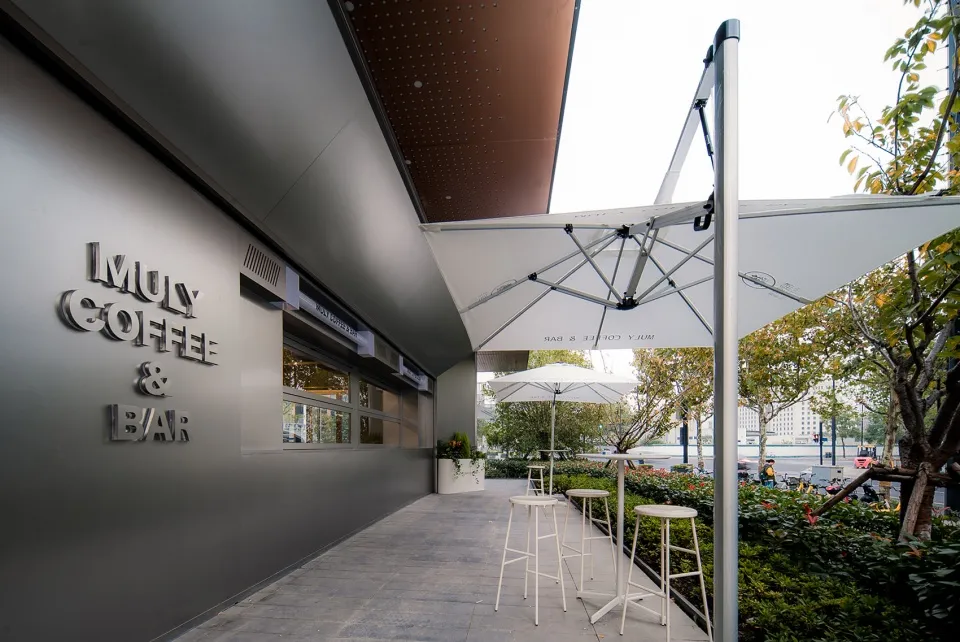 An inviting outdoor coffee shop with a modern design, featuring a large umbrella providing shade and comfort to patrons