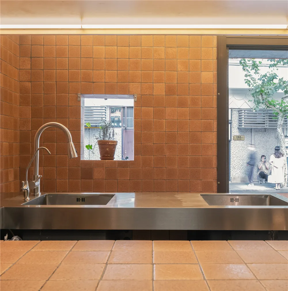 A modern kitchen with two sinks, two potted plants, and a clean, organized atmosphere, featuring tile walls and floors