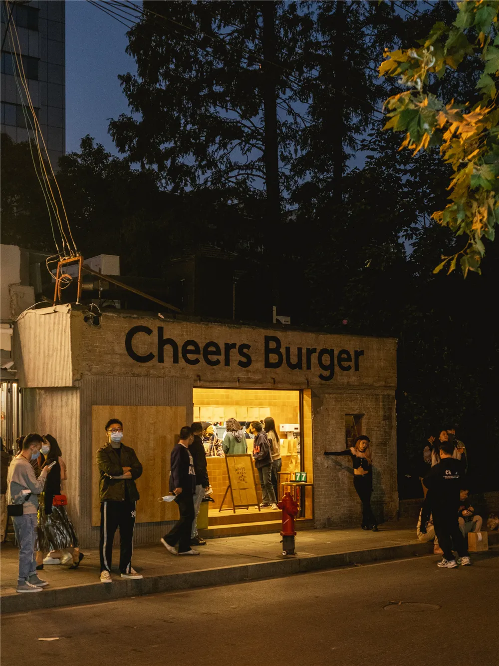 A casual restaurant exterior with a brick wall, people waiting outside the entrance, and a welcoming atmosphere