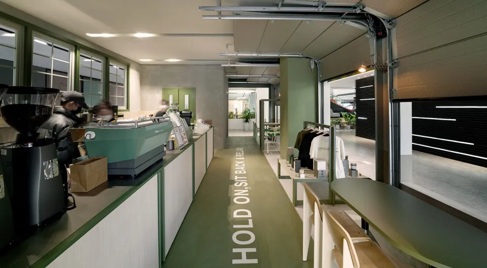 A cozy cafe interior with a green floor, walls, and potted plants, featuring chairs and a welcoming atmosphere
