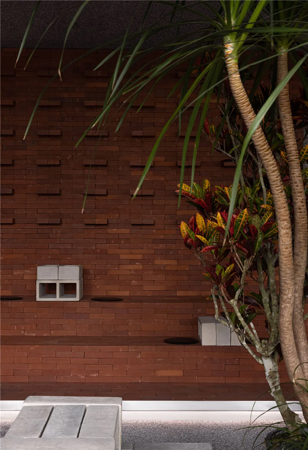 A serene outdoor courtyard with a brick wall featuring a window, two benches, and lush greenery