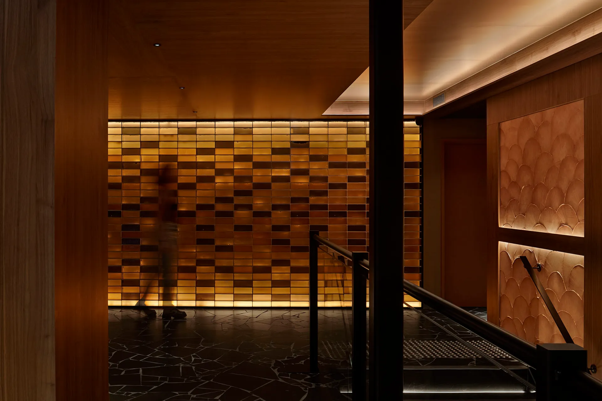 A calm hallway with a wooden door and wooden wall panels, two people walking down the hallway