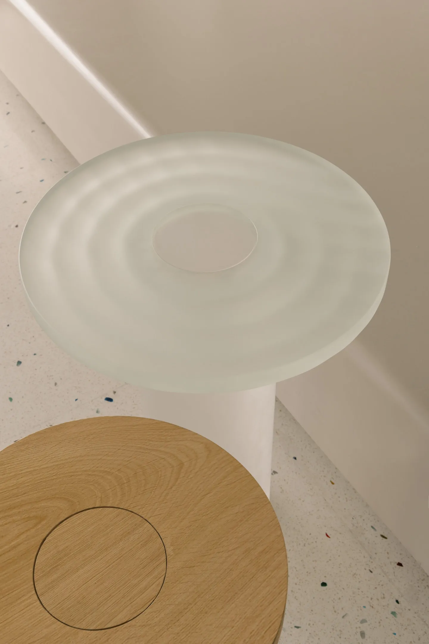 A modern space with a minimalist style featuring a circular glass table on a wooden base in front of a white wall