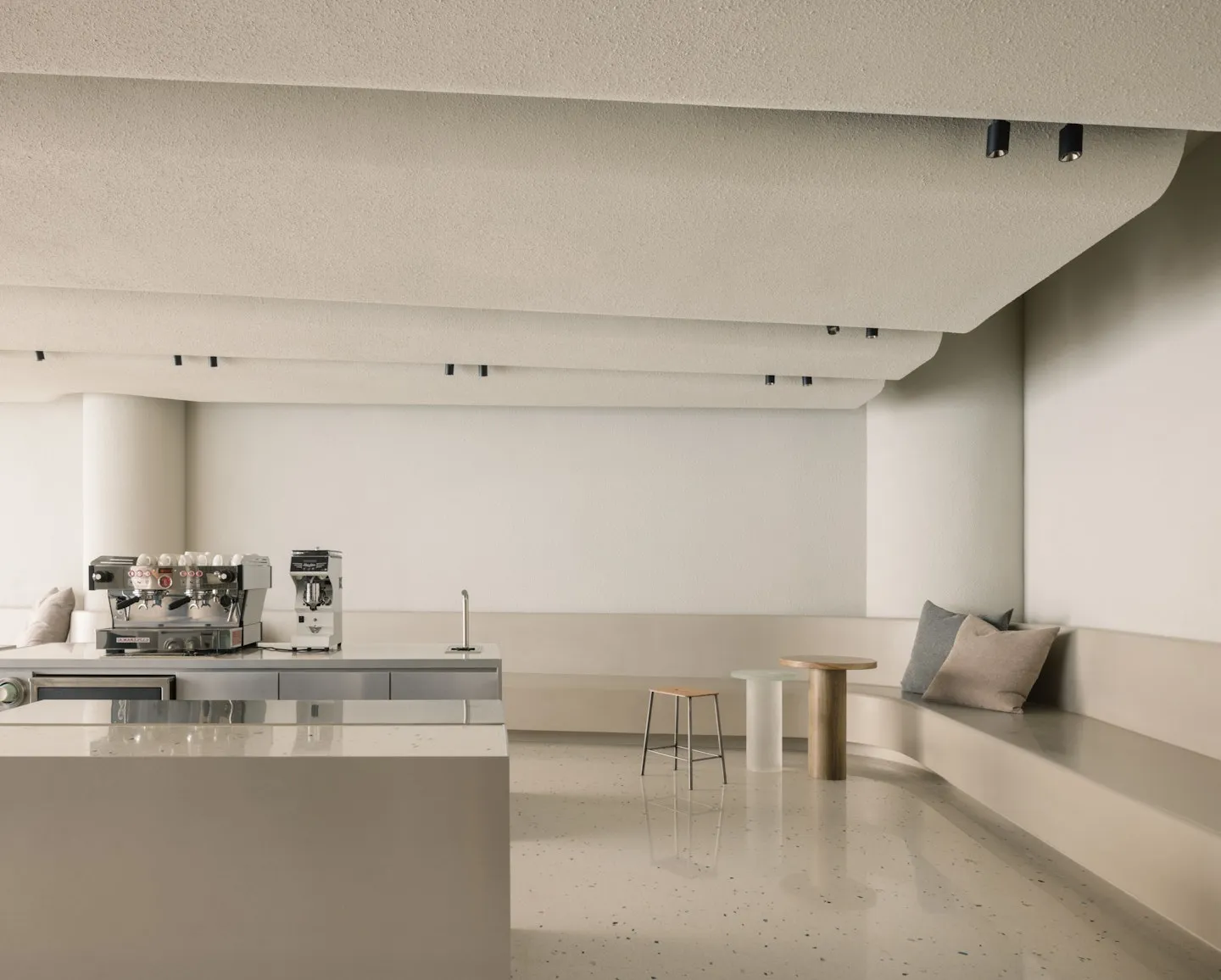 Empty commercial kitchen with white walls and floors, featuring two couches, a dining table, and scattered cups and bottles