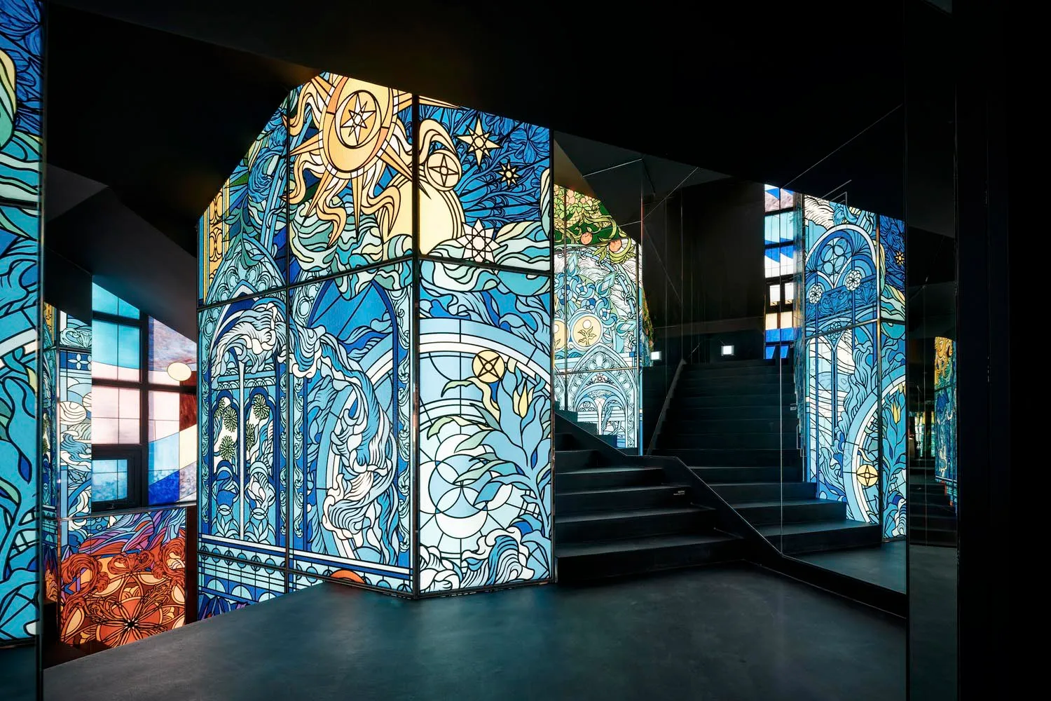 An elegant staircase with a glass railing and metal stairs, surrounded by intricately designed windows in a modern space