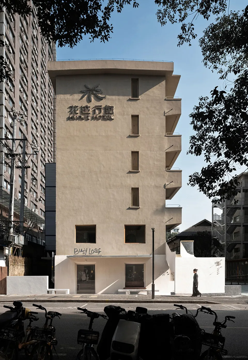 A modern Asian building with a white concrete facade, featuring a large lobby area with people walking and interacting