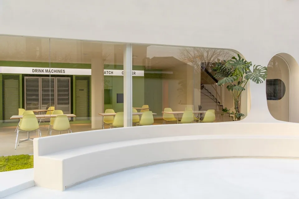A modern restaurant with comfortable seating areas, natural light, and potted plants, featuring various chairs and benches around dining tables