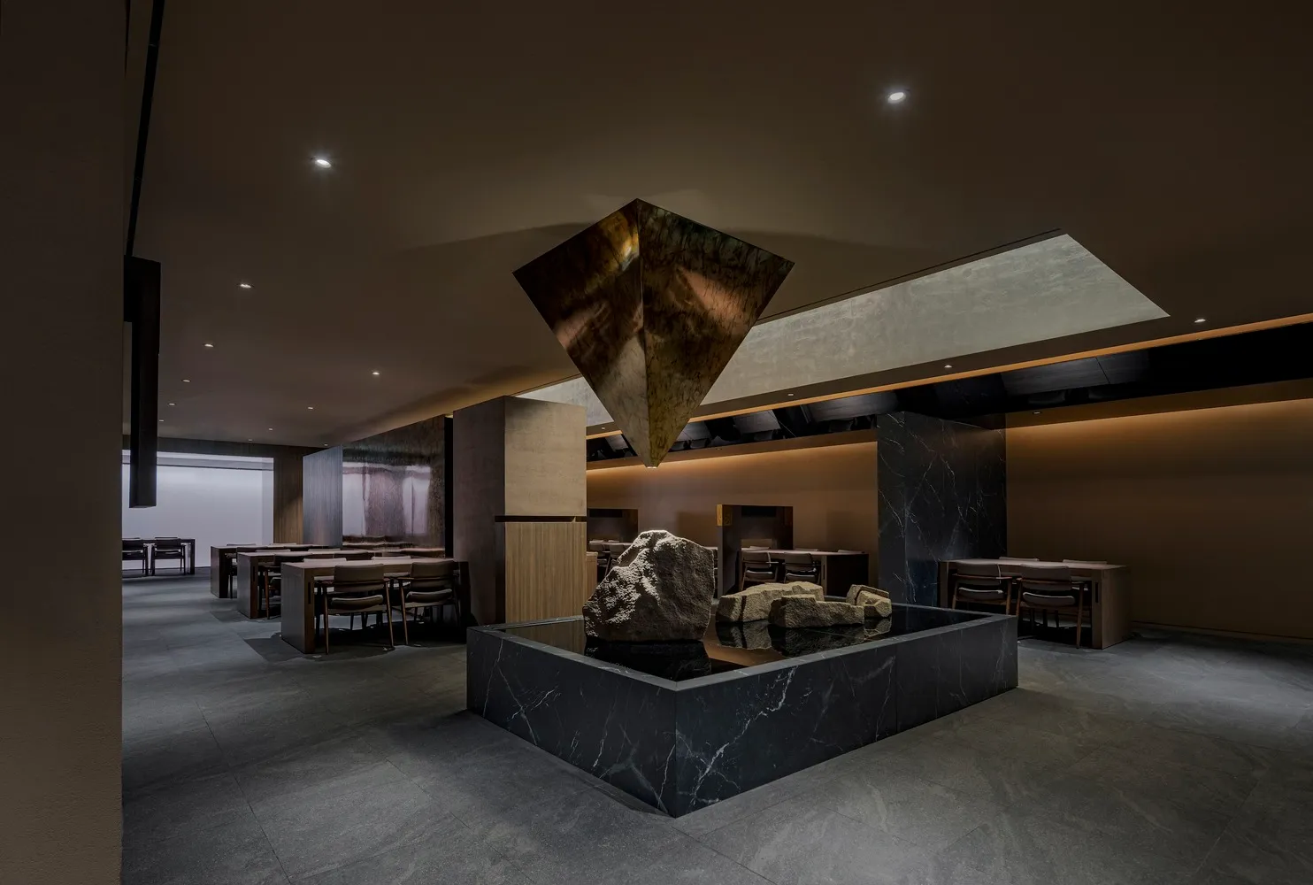 Dimly lit restaurant interior with a stone sculpture centerpiece, surrounded by tables and chairs, with a warm and earthy atmosphere