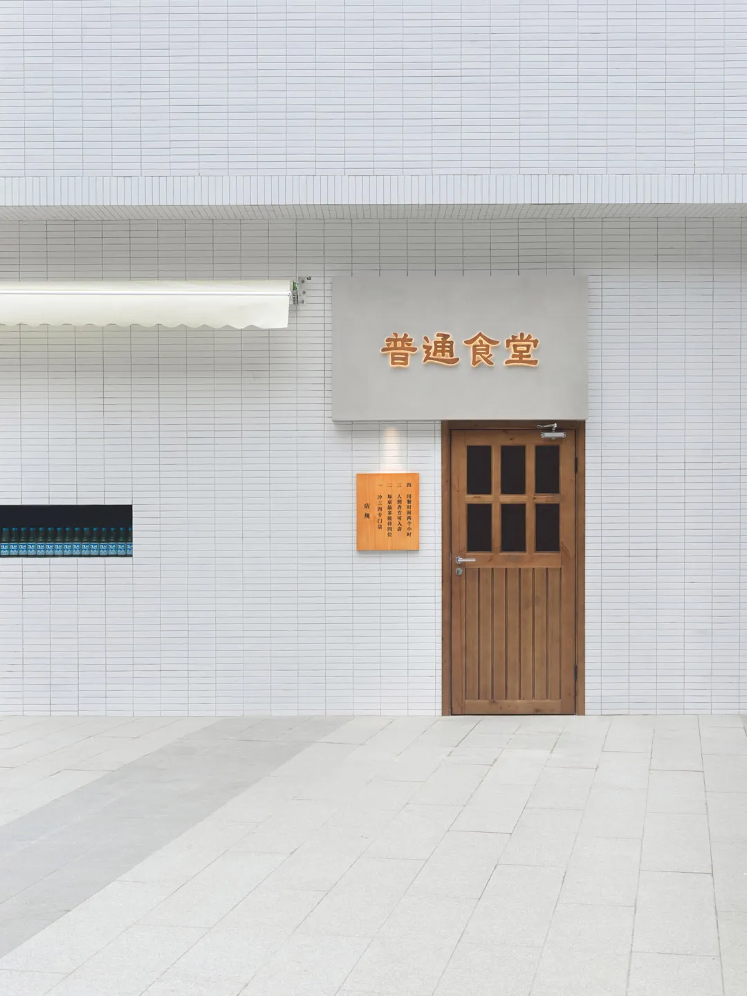 A traditional Asian building with a wooden door featuring Chinese writing, leading to a small room with a sign above it, set against a brick backdrop