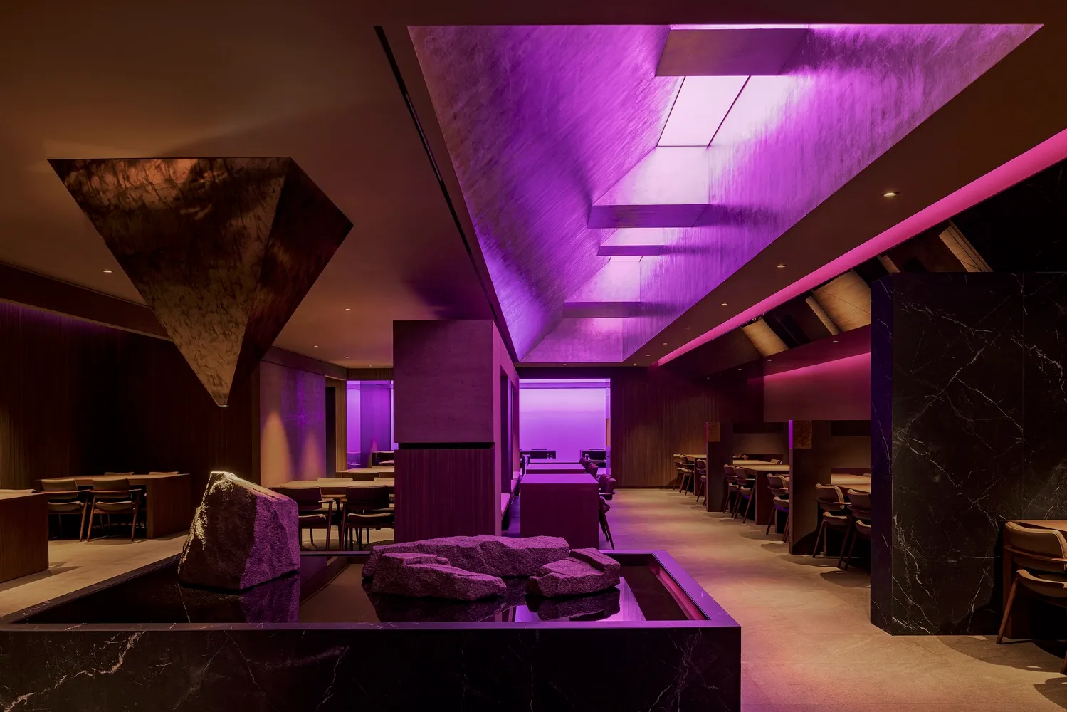 A cozy restaurant dining area with purple walls, ceiling lights, and tables and chairs, creating a warm and inviting atmosphere