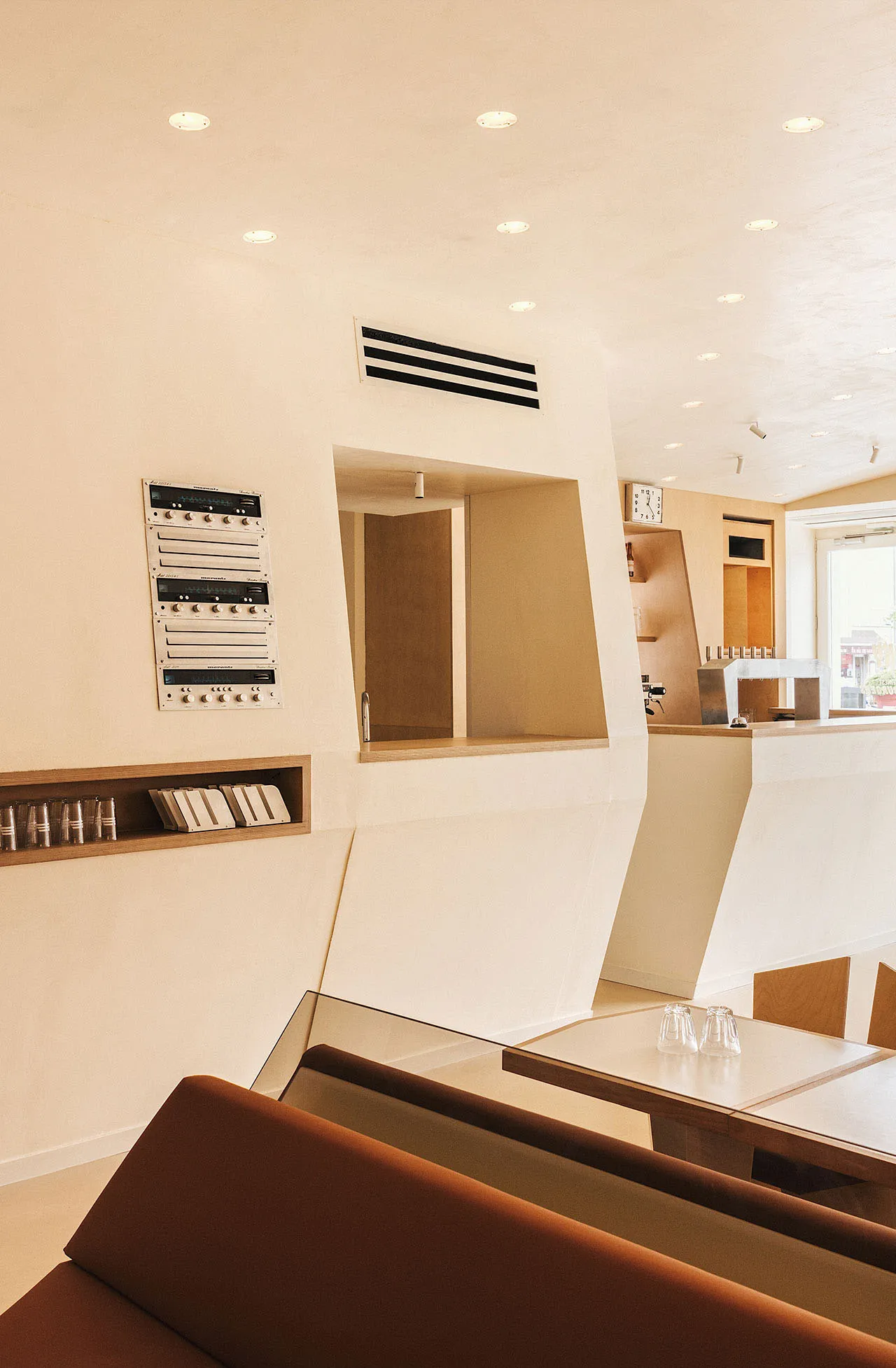 A modern cafe with white walls, wooden furniture, and a counter area with chairs and dining tables, featuring cups and an inviting atmosphere