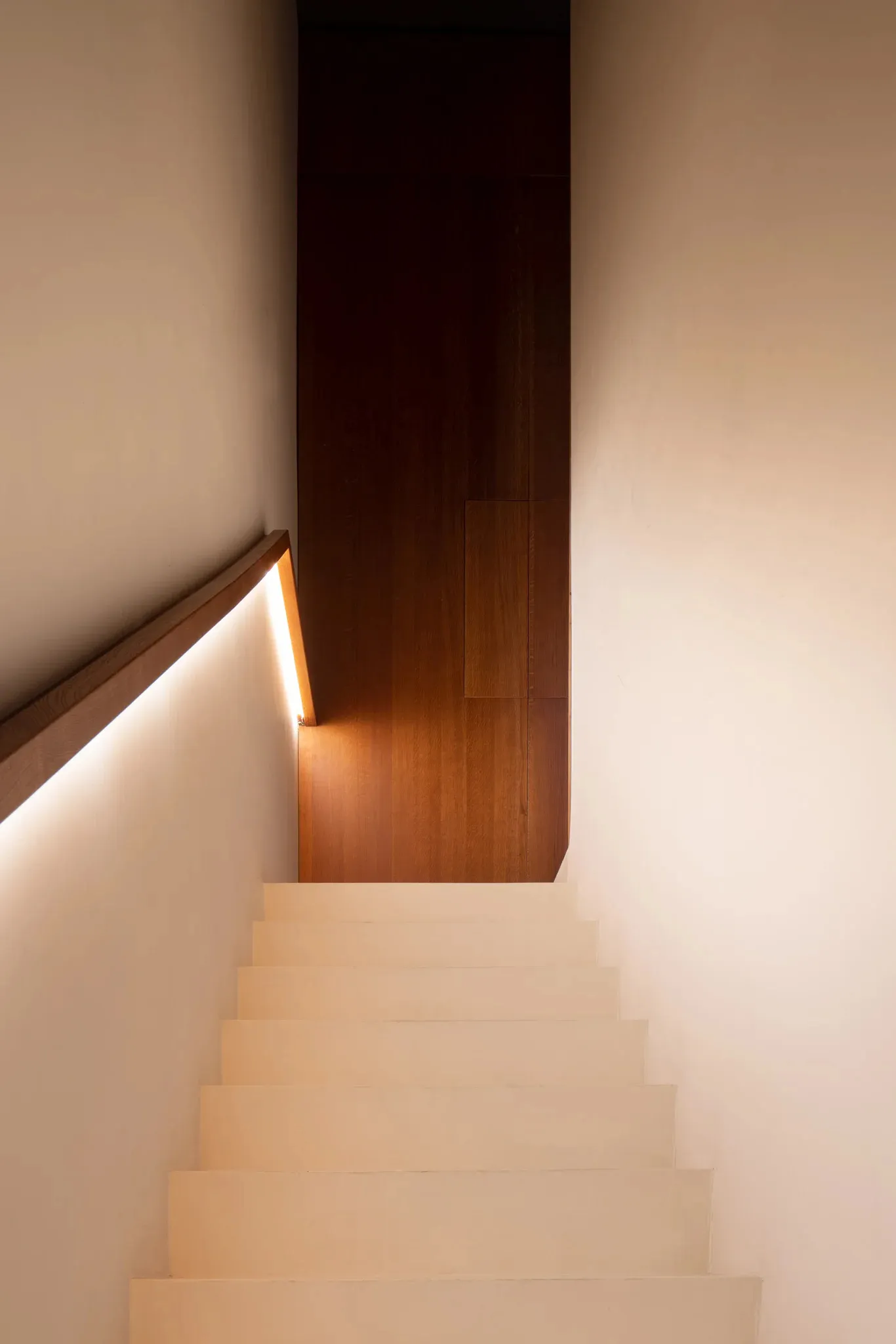 A traditional staircase with wooden steps and a white railing, illuminated by a light at the bottom step, creating a warm atmosphere