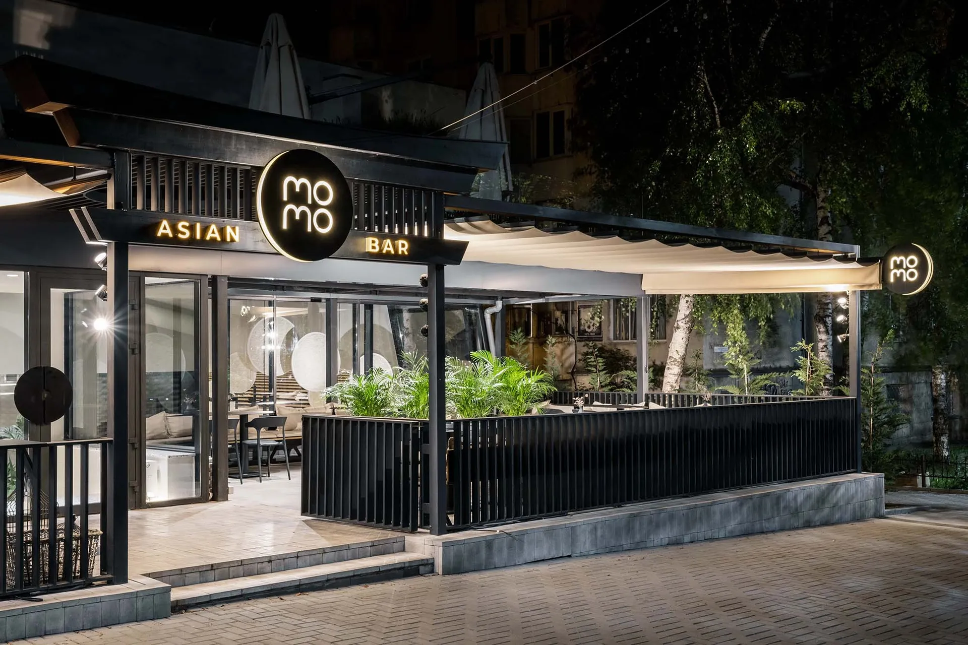 A modern Asian restaurant with a black and white design, featuring tables, chairs, and potted plants, creating an inviting and comfortable atmosphere