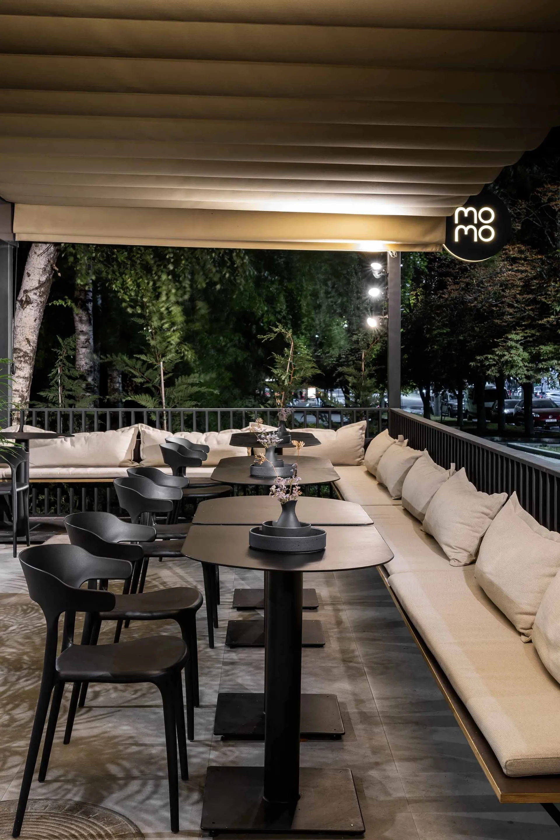 An outdoor dining area at night with tables, chairs, umbrellas, and decorative vases, creating an inviting atmosphere